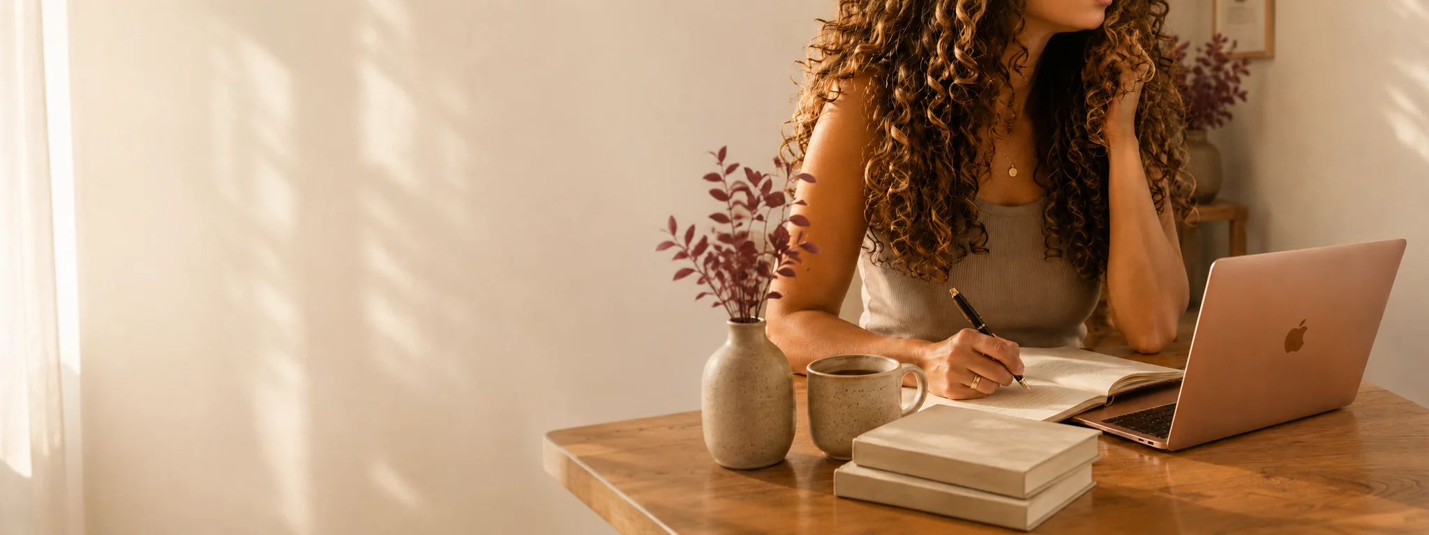 Audra Espinoza, fundadora de Lu PR, en un escritorio de madera escribiendo en un cuaderno junto a una MacBook color oro rosa, luz natural suave, workspace editorial